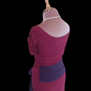 Puede incluir: Un vestido magenta con una faja morada. El vestido tiene un escote redondo y mangas cortas.