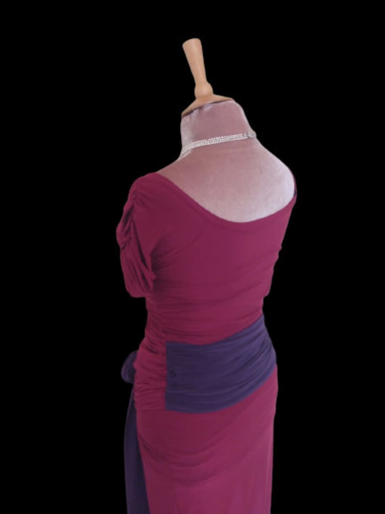 Puede incluir: Un vestido magenta con una faja morada. El vestido tiene un escote redondo y mangas cortas.