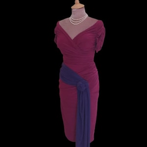 Puede incluir: Un vestido magenta con una faja morada atada a la cintura. El vestido tiene un escote en V y mangas cortas. El vestido est&aacute; en un maniqu&iacute;.
