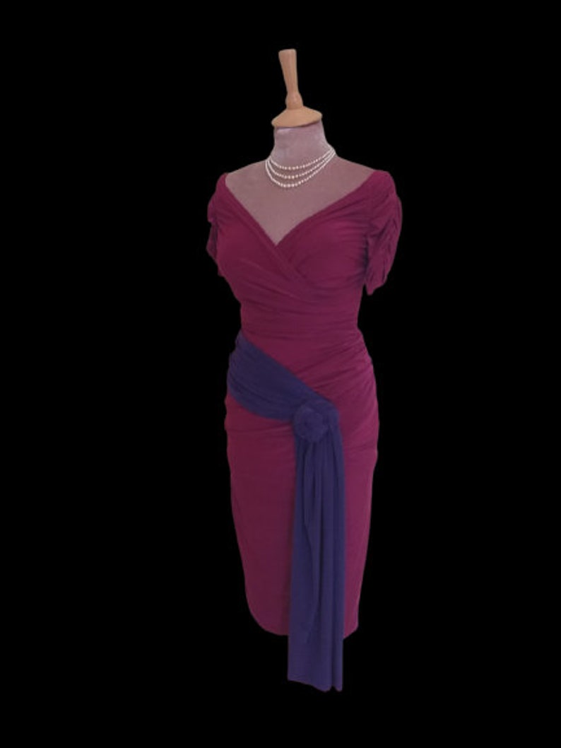 Puede incluir: Un vestido magenta con una faja morada atada a la cintura. El vestido tiene un escote en V y mangas cortas. El vestido est&aacute; en un maniqu&iacute;.