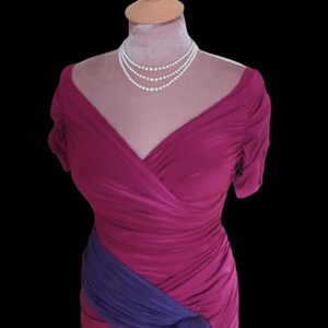Puede incluir: Un vestido magenta con una faja morada anudada a la cintura. El vestido tiene un escote en V y mangas cortas. El vestido est&aacute; en un maniqu&iacute; y tiene un collar de perlas.