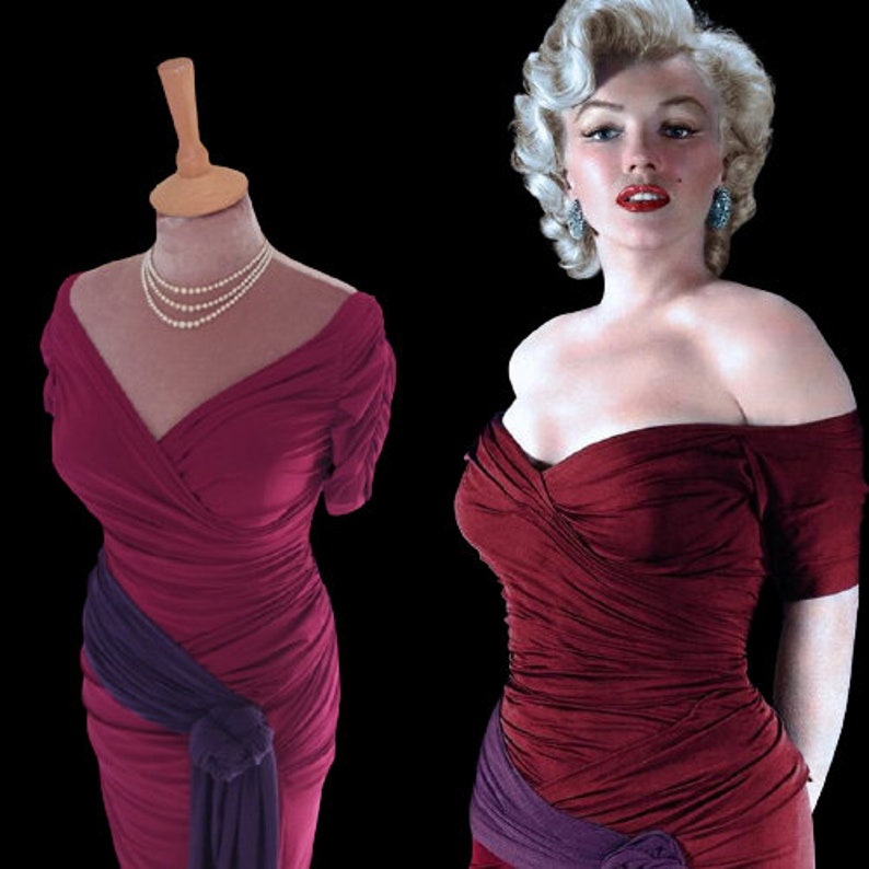 Puede incluir: Un vestido rojo sin tirantes con una faja morada y un escote drapeado. El vestido est&aacute; en un maniqu&iacute; con un collar de perlas.
