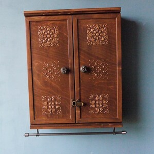 May include: A dark brown wooden cabinet with two doors and a metal bar underneath. The doors have intricate carved designs and metal knobs.