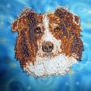May include: Embroidered image of a brown and white dog with a fluffy white beard. The dog's fur is detailed with brown, white, and black embroidery stitches. The background is a blue and white tie-dye pattern.