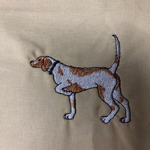 May include: Embroidered image of a brown and white dog with a black collar on a beige fabric background.