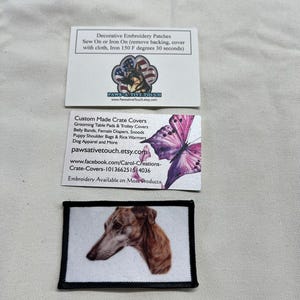 May include: A rectangular patch featuring a brown and white dog portrait with a black border, positioned below two white business cards. The top card displays a paw print logo and instructions for iron-on patches. The middle card shows a purple butterfly.