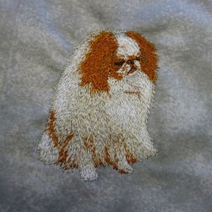 May include: Embroidered image of a white and orange Japanese Chin dog with fluffy fur.