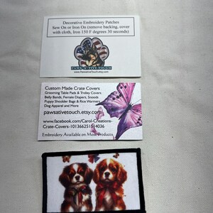 May include: Two rectangular business cards and one rectangular embroidered patch. The top card features a German Shepherd in a paw print. The middle card shows a purple butterfly. The bottom patch displays two Cavalier King Charles Spaniels.