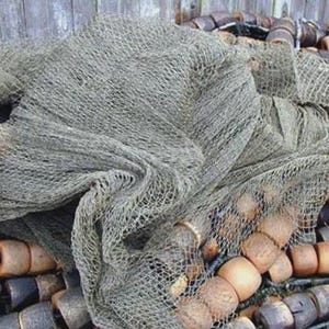 Puede incluir: Una pila de flotadores marrones y blancos cubiertos con una red de pesca gris. La red está hecha de un material tejido y tiene una textura rugosa.