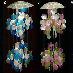 Puede incluir: Cuatro carillones diferentes hechos de conchas iridiscentes. Cada carillón tiene un esquema de color diferente: morado y dorado, azul y verde, rosa y verde, y marrón y dorado.