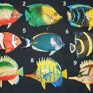 Pode incluir: Nove figurinhas de peixes de madeira pintadas à mão e coloridas. Cada peixe é único com cores, padrões e designs diferentes. Os peixes são numerados de 1 a 9.