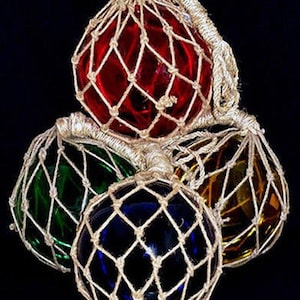 May include: Set of four glass fishing floats, each encased in a natural twine net. The floats are red, green, blue, and yellow. The floats are 8 inches in diameter.
