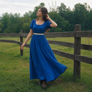 Könnte beinhalten: Ein bodenlanges, königsblaues Kleid mit kurzen Puffärmeln, einem weiten Ausschnitt und einem figurbetonten Oberteil. Das Kleid hat ein schmales, helles horizontales Band an der Taille und einen langen, fließenden Rock, der bis zu den Knöcheln reicht.