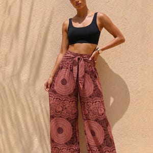 May include: A black scoop-neck crop top paired with wide-leg trousers featuring a dark red and black circular mandala-style pattern. The trousers have a high-waisted design with a matching fabric tie at the center of the waistband.