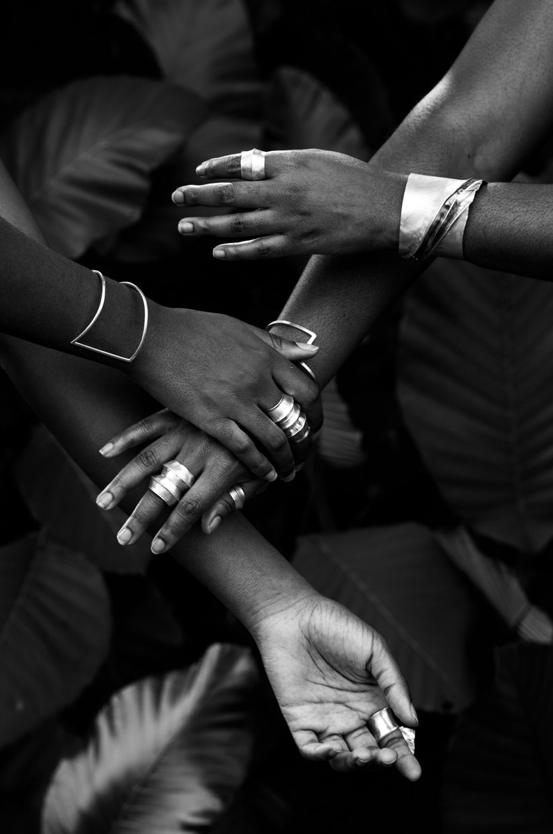 Four hands reaching toward and clasping each other adorned in silver rings and bracelets.