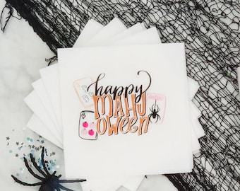 May include: A set of white party supplies featuring the text Happy Mahj Oween in orange and black, including a scalloped edge towel, two foam cups, a stack of napkins, and three round cookies, all decorated with mahjong tile and spider graphics.