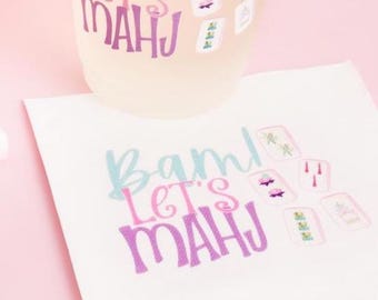 May include: A translucent plastic cup and a white paper napkin, both featuring the text "Bam! Let's MAHJ" in blue, pink, and purple, accompanied by small illustrations of mahjong tiles in various colors.