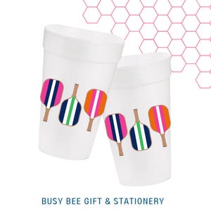 May include: Two white foam cups decorated with colorful pickleball paddle designs. The paddles feature pink, orange, blue, and green stripes. The text "BUSY BEE GIFT & STATIONERY" is at the bottom.