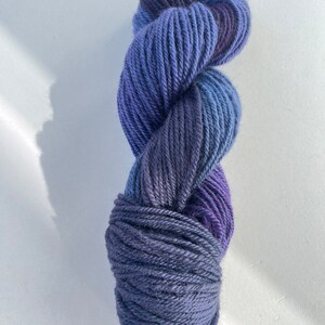 Peut inclure: Une pelote de laine bleue et violette avec un effet dégradé. La laine est douce et moelleuse, et elle serait parfaite pour le tricot ou le crochet.