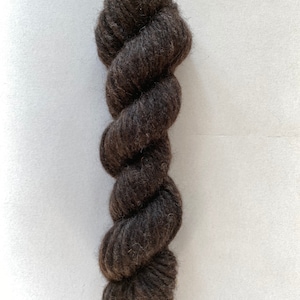 Peut inclure: Une pelote de laine de couleur brun foncé, avec une texture duveteuse.
