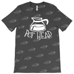 May include: A dark gray t-shirt with a white graphic of a coffee pot and the text "Pot Head". The shirt is covered in a repeating pattern of the word "SLINGSHOT" in a lighter gray color.