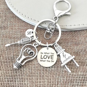 Pode incluir: Chaveiro prateado com um charme de lâmpada, chave de fenda e plugue elétrico. O charme tem o texto "Do What You LOVE What You Do".
