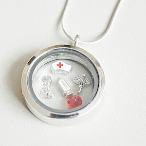 May include: Silver locket necklace with a red and white nurse's cap charm, a stethoscope, a syringe, a caduceus, and a red gemstone.