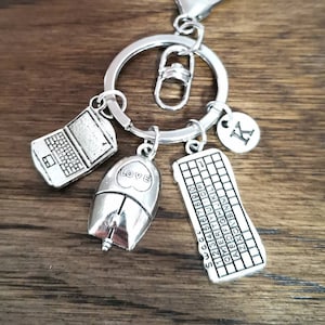 Puede incluir: Llavero de plata con un portátil, un ratón, un teclado y un dije con la letra K. El dije del ratón tiene la palabra "LOVE" en él.