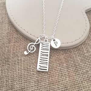 May include: Silver necklace with a piano keyboard charm, a treble clef charm, and a charm with the letter "P" hanging from it.