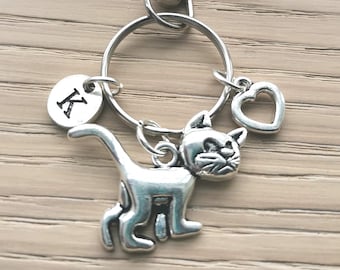 May include: Silver keychain with a cat charm, a heart charm, and a round charm with the letter K.