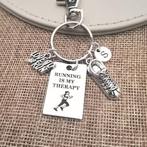 May include: Silver keychain with a charm that says "Running is my therapy" and a running figure. The keychain also has a charm that says "Love to Run" and a shoe charm. The keychain has a silver letter "S" charm.