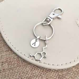 May include: Silver keychain with a letter A charm and a dopamine molecule charm.