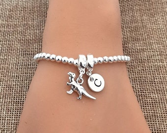 May include: Silver charm bracelet with a dinosaur and initial charm. The bracelet is made of small silver beads and has a sliding clasp.
