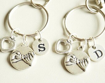 May include: Two silver keychains with charms. Each keychain has a round ring, a heart-shaped charm, a round charm with a letter, and a charm depicting clasped hands. One keychain has the letter "S", the other has "D".