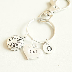 May include: Silver keyring with a beer bottle cap charm, a heart charm engraved with the word "Dad", and a charm engraved with the letter "O".