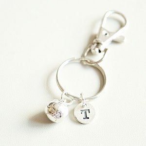 May include: Silver keychain with a soccer ball charm and a letter 'T' charm.