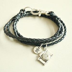 Peut inclure: Un bracelet en cuir tressé noir avec un charme de caméra argenté et un charme argenté avec la lettre "E" dessus.