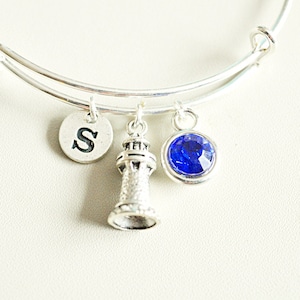 May include: Silver charm bracelet with a lighthouse charm, a blue crystal charm, and a charm with the letter "S" on it.