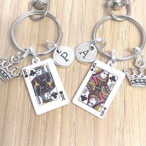 Op de afbeelding: Twee zilveren sleutelhangers met een speelkaartenhanger, een met de koning van klaveren en de andere met de koningin van klaveren. Elke hanger heeft een kleine zilveren kroon en een zilveren schijf met de letter 'P' en 'A' erop.