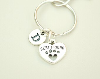 May include: Silver keychain with a round charm with the letter "D" and a heart-shaped charm that says "BEST FRIEND" with a paw print design. The keychain is on a silver ring.