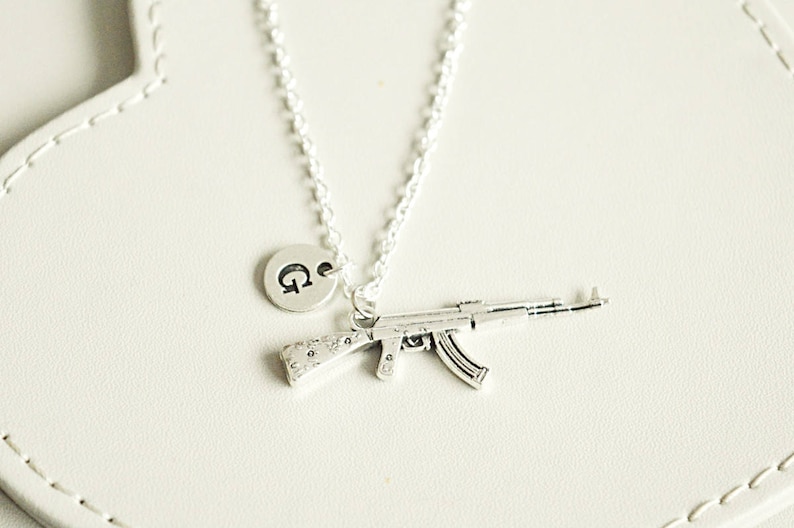 May include: A silver necklace with a charm of a small gun and a letter 'G' charm.
