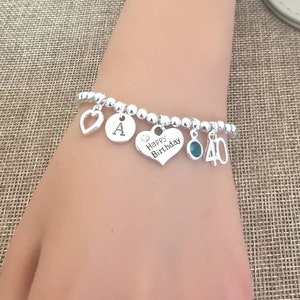 May include: Silver charm bracelet with a heart charm that says "Happy Birthday", a charm with the letter "A", a charm with a turquoise stone, and a charm with the number "40".