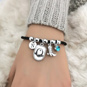 May include: A black elastic bracelet with silver charms, including a cowboy hat, a cowboy boot, a letter 'N' charm, and a blue crystal charm.