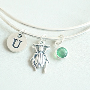 Pode incluir: Um bracelete de prata com uma gema verde, um amuleto de prata de besouro e um amuleto de prata com a letra U.
