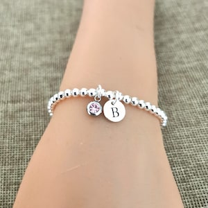 Puede incluir: Un brazalete de plata con cuentas, un dije de cristal rosa y un dije de plata con la letra "B" grabada.