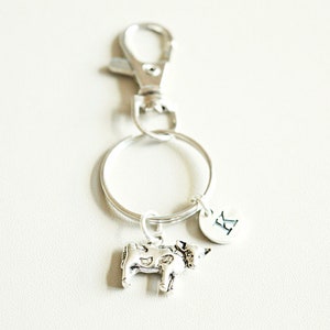 May include: Silver cow keychain with a silver ring and a silver clip. The keychain also has a silver charm with the letter "R" on it.