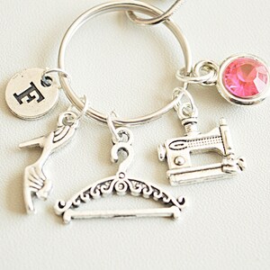 May include: Silver charm keyring with a pink rhinestone, a sewing machine, a hanger, a high heel shoe, and a charm with the letter "E".