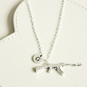 May include: A silver necklace with a charm of a small silver gun and a silver disc with the letter "G" on it.