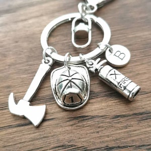 May include: Silver firefighter keychain with a fire hat, axe, fire extinguisher, and a letter B charm. The fire hat has the number 1 on it. The fire extinguisher has the word "FIRE" on it.
