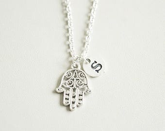 Peut inclure: Collier en argent avec un pendentif en forme de main de Hamsa et un petit pendentif rond avec la lettre 'S'.